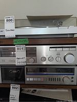 Side view of vintage turntable, stereo receiver, and tape player units with lot tags. Receiver lot tag number 801 visible.
