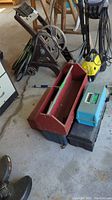 Four toolboxes in varying condition: classic red wood toolbox on top, blue plastic toolbox labeled Advantage, red metal toolbox, and black plastic tackle box with fishing tackle inside.