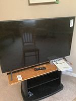 Front view of 50" Samsung TV on wooden table stand showing bezel, screen and included accessories