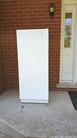Front view of closed white upright freezer showing exterior door and bottom vent.