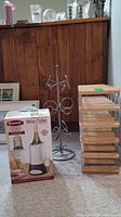 Wooden wine rack, metal wine stand, and boxed Bravetti Wine Chiller placed on carpet with wooden cabinet backdrop.