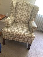 Front view of the wing chair showing the beige fabric with diamond pattern, wingback design, and wooden legs.