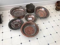 Overview of six antique brass pots and bowls placed on floor showing size differences and worn patina