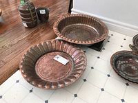 Two large antique brass containers on floor and wood table, showing size and condition with patina and wear
