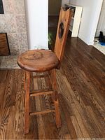 Side and angle view of the antique solid wood stool showing round seat, backrest with circular cutout, legs and stretchers on hardwood floor.