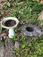 Photo showing the bird bath base and damaged top on ground with surrounding greenery and rocks