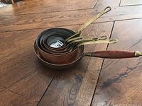 Seven copper pots nested inside each other showing handles and copper exteriors.