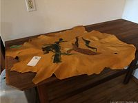 Full view of the cowhide laid flat on a wooden table showing the painted hawk and overall shape of the hide.
