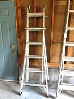 Front view of aluminum multi-task ladder in A-frame position in a garage setting next to blue door and plywood wall.