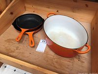 Overview of two cast iron frying pans and one large oval roaster with orange handles on a wooden surface.
