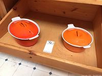 Two round Le Creuset casseroles with lids placed side by side, showing orange gradient colors on exterior.