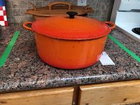 Orange Le Creuset Dutch oven with lid sitting on countertop, showing shape and exterior condition.