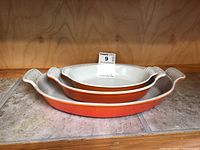 Three stacked Le Creuset oval baking dishes, showing size variation and orange exterior with white interior.