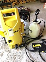 Yellow Karcher pressure washer with attached hose, and two white Stand-N-Spray sprayers nearby on a concrete floor.