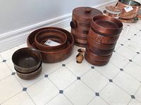 Two large segmented wooden salad bowls stacked, six smaller wooden bowls stacked, two small carved wooden bowls, and a wooden item with double spouts on the floor