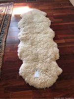 Full view of the long sheepskin rug laid out on a wooden floor, showing natural cream wool and approximate size.