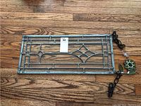 Full view of one rectangular stained glass panel lying on wooden floor, showing diamond-shaped central design and metal framing