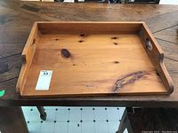 Full view of rectangular wooden serving tray with handles on each side placed on a wooden table.