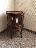 Full side view of ornate round wooden table with beveled glass panels and carved Queen Anne legs.