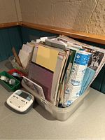 Plastic bin filled with various card stocks and paper sheets with a white Brother P-touch 90 label maker placed in front.