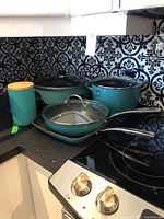 Full view of cookware set and canisters on kitchen counter, showing turquoise exterior and glass lids.