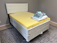 Side view of the assembled double bed with yellow mattress topper and linens stacked on top