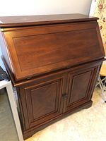 Closed wooden drop front desk showing smooth wood finish and double door closed storage area below.