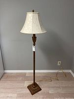 Full view of the ornate floor lamp showing metal base, wooden column, and off-white shade