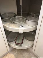 Three round glass and three French White covered casserole dishes with lids, along with other glass bakeware on two rotating shelves.