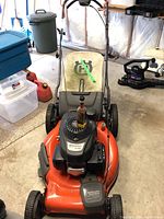 Front view of Husqvarna lawn mower showing orange deck, Honda engine, and handlebar with padded backrest.