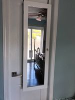 Front view of white wooden jewelry cabinet hung over a door with a full-length mirror on the front.