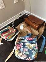 Photo showing three ladies purses on dark hardwood floor: Patricia Nash brown embossed leather purse, Suo Ya Te floral fabric purse, and colorful striped Giani Bernini purse.