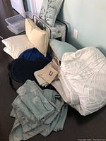 Full view of bedding, pillows, duvet covers, and linens piled on floor showing colors and textures