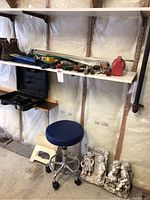 Shelf holding various hand tools, black empty tool case, blue rolling stool below, small white folding step stool nearby