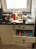 Overview of various kitchen items including glassware, mugs, a cutting board, and small appliances on countertop with open drawer showing storage wraps.