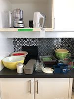 Full overview of lot items on kitchen counter and shelf including bowls, appliances, pans, and containers
