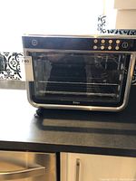 Front view of Ninja Air Oven on countertop showing outer appearance, transparent glass front, and control buttons on top panel.