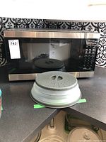 Front view of Panasonic microwave oven with splatter cover in front showing microwave exterior and part of kitchen background.