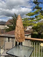 Photo of closed Caribbean style patio umbrella with faux thatch canopy over a glass patio table.