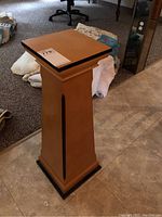 Full view of the wooden pedestal showing the top, body, and base with black accents.