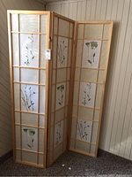 Full view of the privacy screen showing its three hinged wooden panels with framed sections of painted floral paper designs.