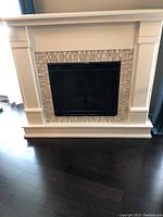 Full front view of white mantel and black firebox insert on dark wood floor