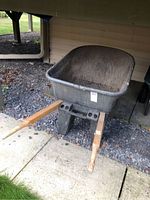 Front angled view showing the plastic basin, wooden handles, and leg support on the wheelbarrow.
