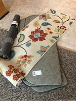 Photo showing rolled grey accent mat, floral runner, and four gray anti-fatigue mats stacked underneath