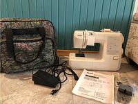 Sewing machine with travel bag, foot pedal power cord, owner's manual, and some sewing notions on floor.