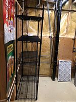 Full view of the black metal shelving unit in a basement setting, showing its tall stature and four shelves.