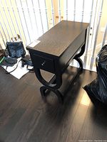 Photo of black side table from an angle showing top and side, with curved legs and drawer visible.