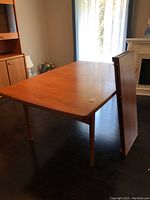 Full view of rectangular teak table without leaves; one leaf leaning against side