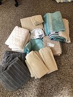 Overview of assorted towels and bath mats in neutral colors on carpeted floor
