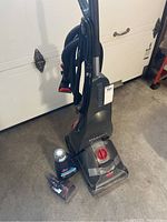 Bissell StainPro carpet cleaner with bottle of detergent and brush attachment on concrete floor in front of garage door.